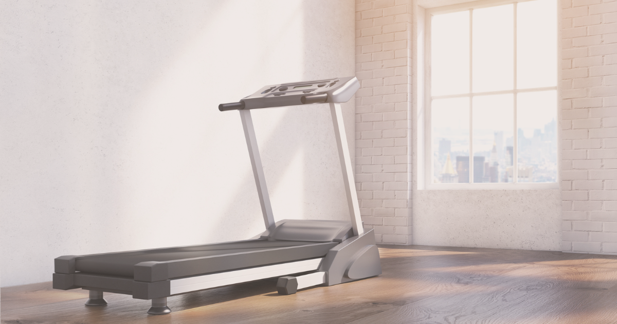 A modern treadmill is placed on a wooden floor in a room with a large window and white brick walls.